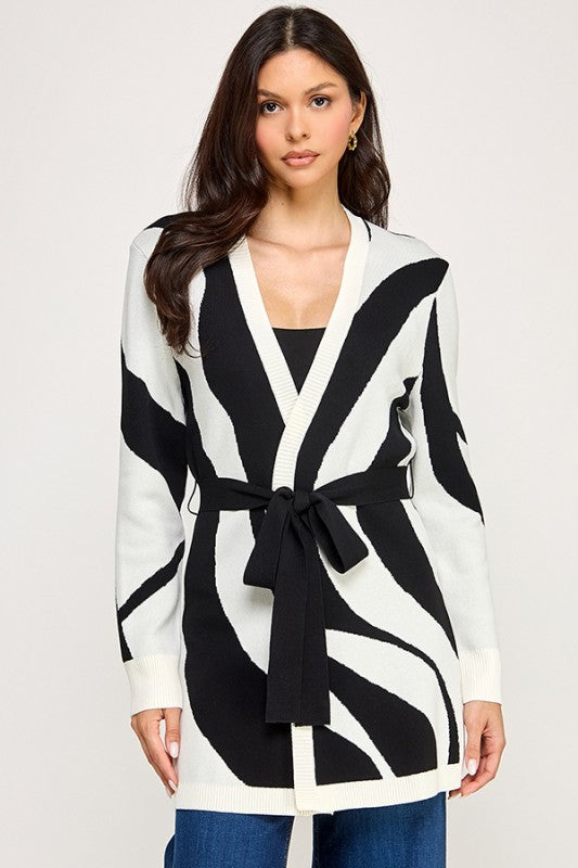 Woman wearing a black and white striped cardigan with a belt on a plain background