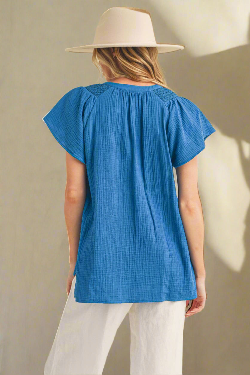 Woman wearing a blue top and white pants with a beige hat on a plain background