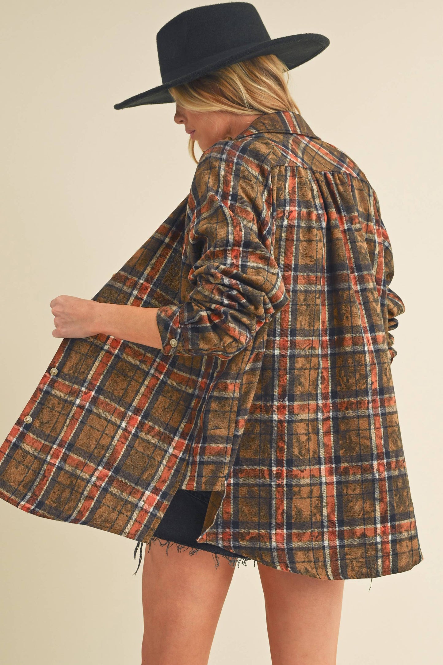 Person wearing a plaid jacket and black hat on a beige background