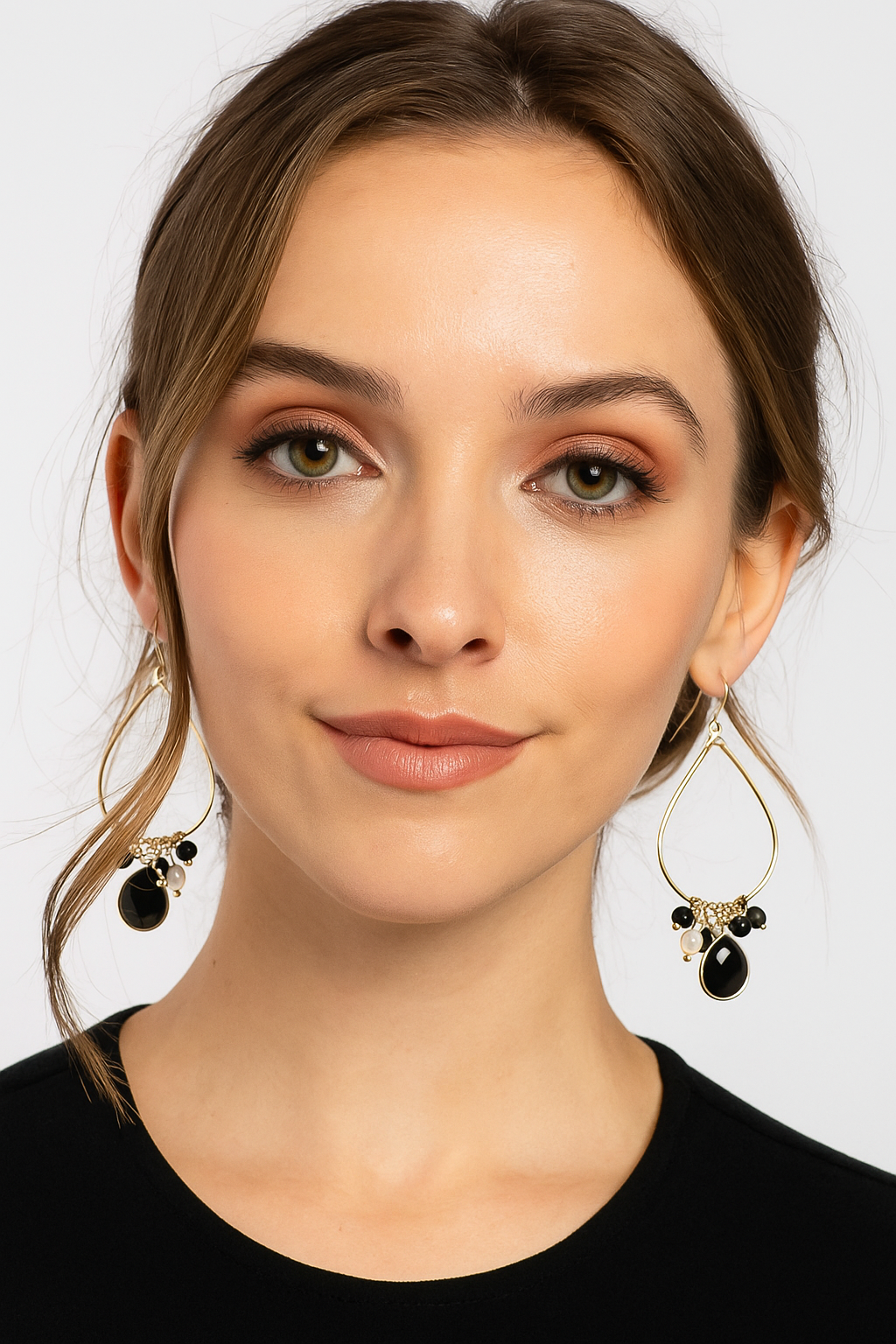 Woman wearing gold earrings with black stones on a plain background
