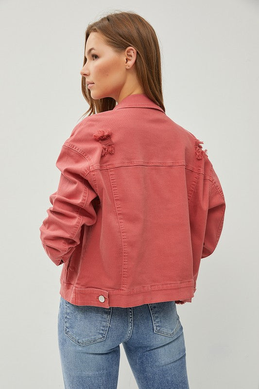 Woman wearing a rust denim jacket and blue jeans on a light gray background