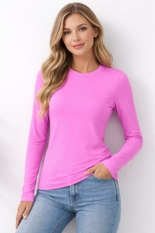 Woman wearing a bright mauve long-sleeve top and blue jeans against a white background