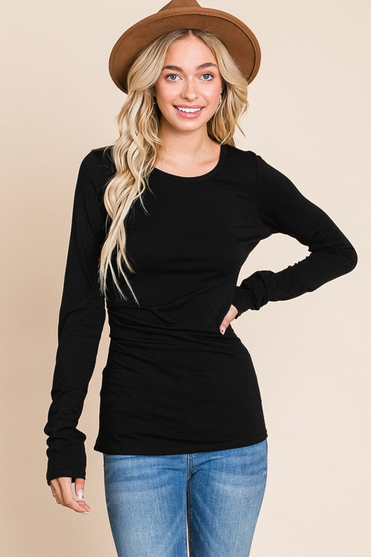Woman wearing a black long-sleeve top and blue jeans with a beige background
