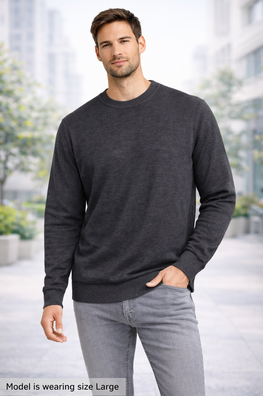 Man wearing a dark gray sweater and light gray pants standing outdoors with blurred background
