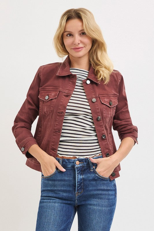 Woman wearing a maroon jacket, striped shirt, and blue jeans on a light gray background