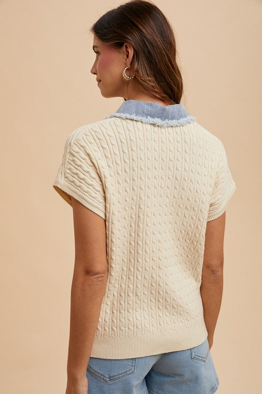 Woman wearing a cream knitted vest over a blue shirt on a beige background