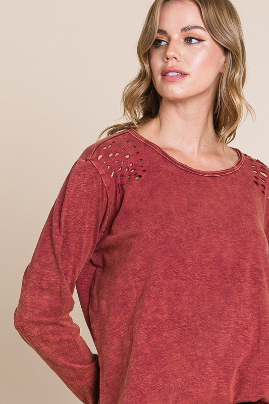 Woman wearing a red long-sleeve top with cut-out shoulders against a beige background