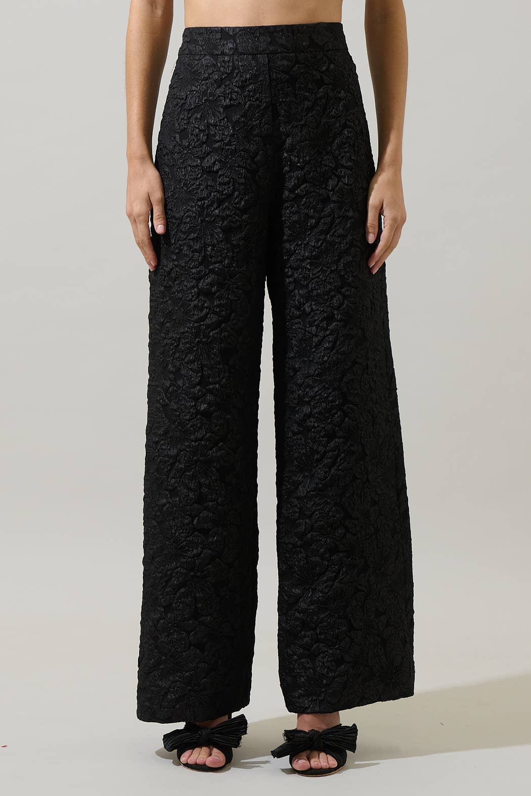Person wearing black textured pants on a plain background