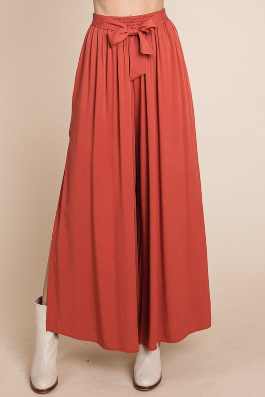 Rust pant with a tie waist worn with white boots on a beige background