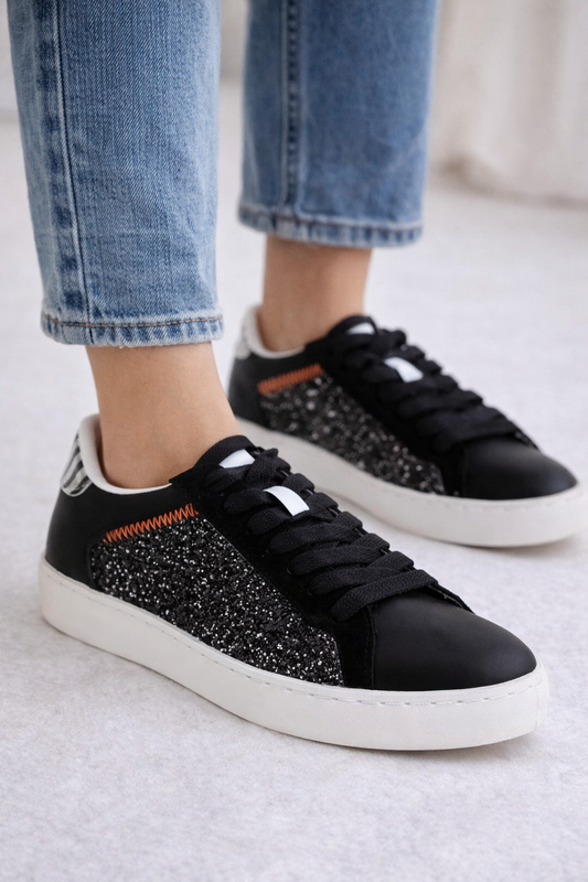 Black glittery sneakers with white soles worn with blue jeans on a light background