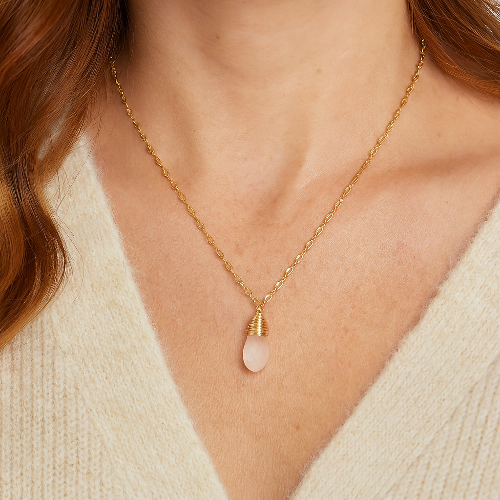 Gold necklace with a clear stone pendant on a person wearing a beige sweater.