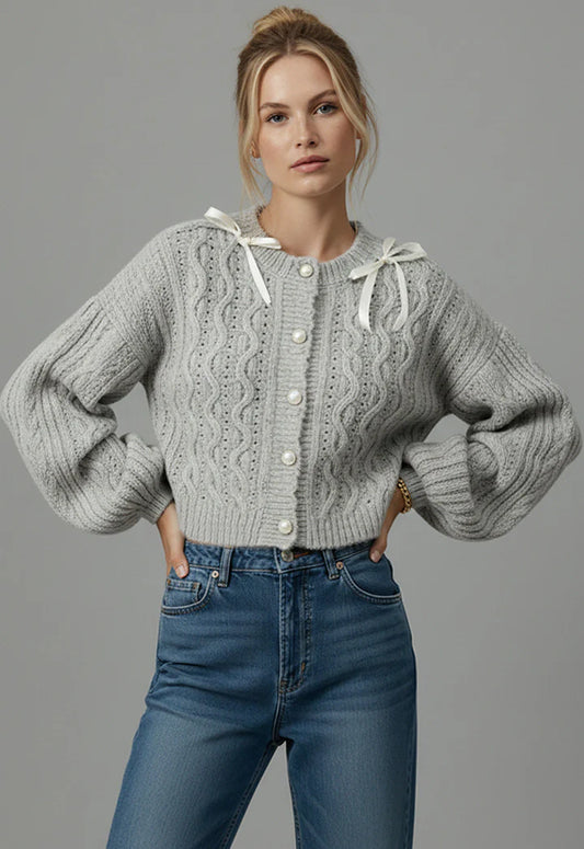 Woman wearing a gray cable knit sweater and blue jeans against a gray background