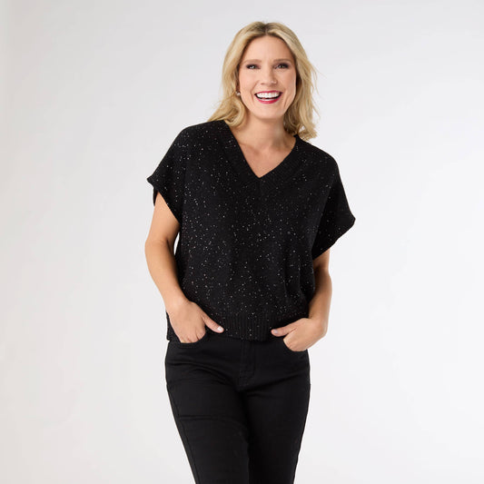 Woman wearing a black speckled top and black pants on a white background