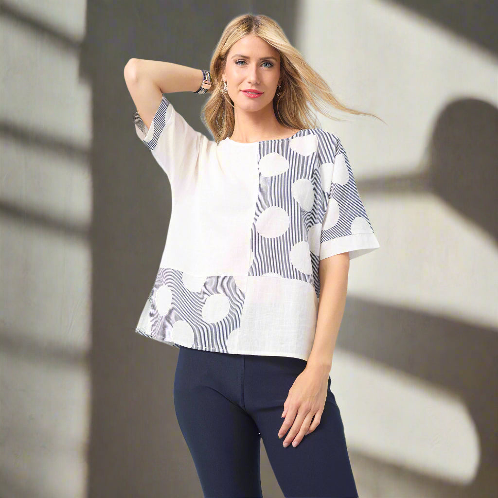 Woman wearing a polka dot blouse and dark pants against a light blue background