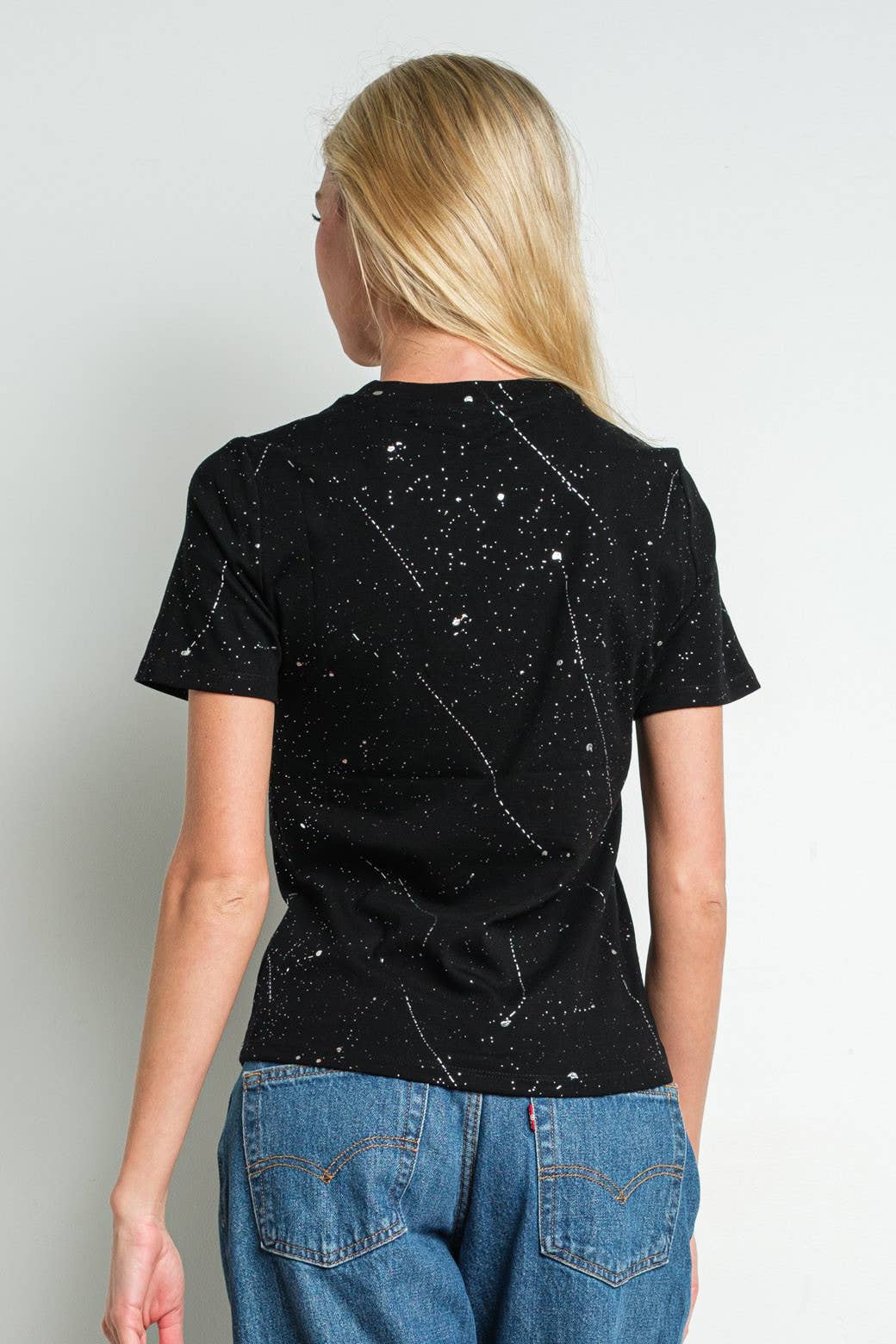Person wearing a black t-shirt with pattern and blue jeans on a white background