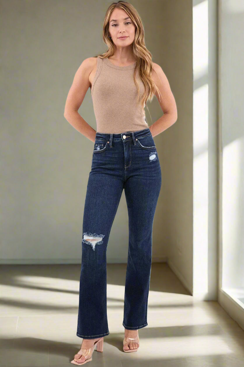 Woman wearing blue jeans and a beige tank top on a white background