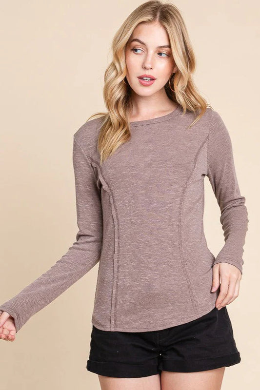 Woman wearing a brown long-sleeve top and black shorts on a beige background