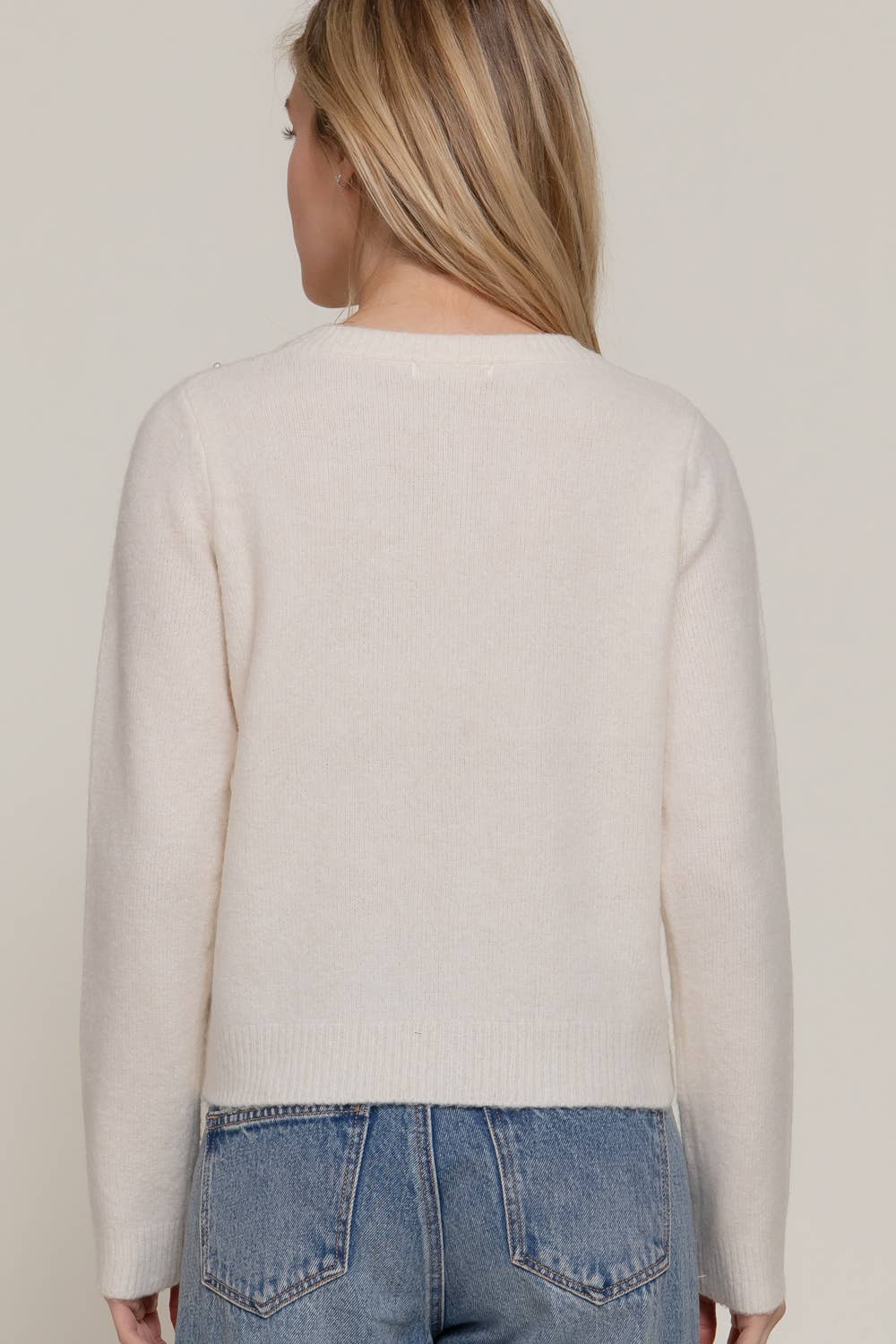 Person wearing a beige sweater and blue jeans against a plain background
