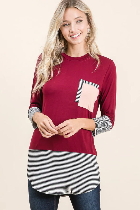 Woman wearing a burgundy long-sleeve top with striped hem on a beige background