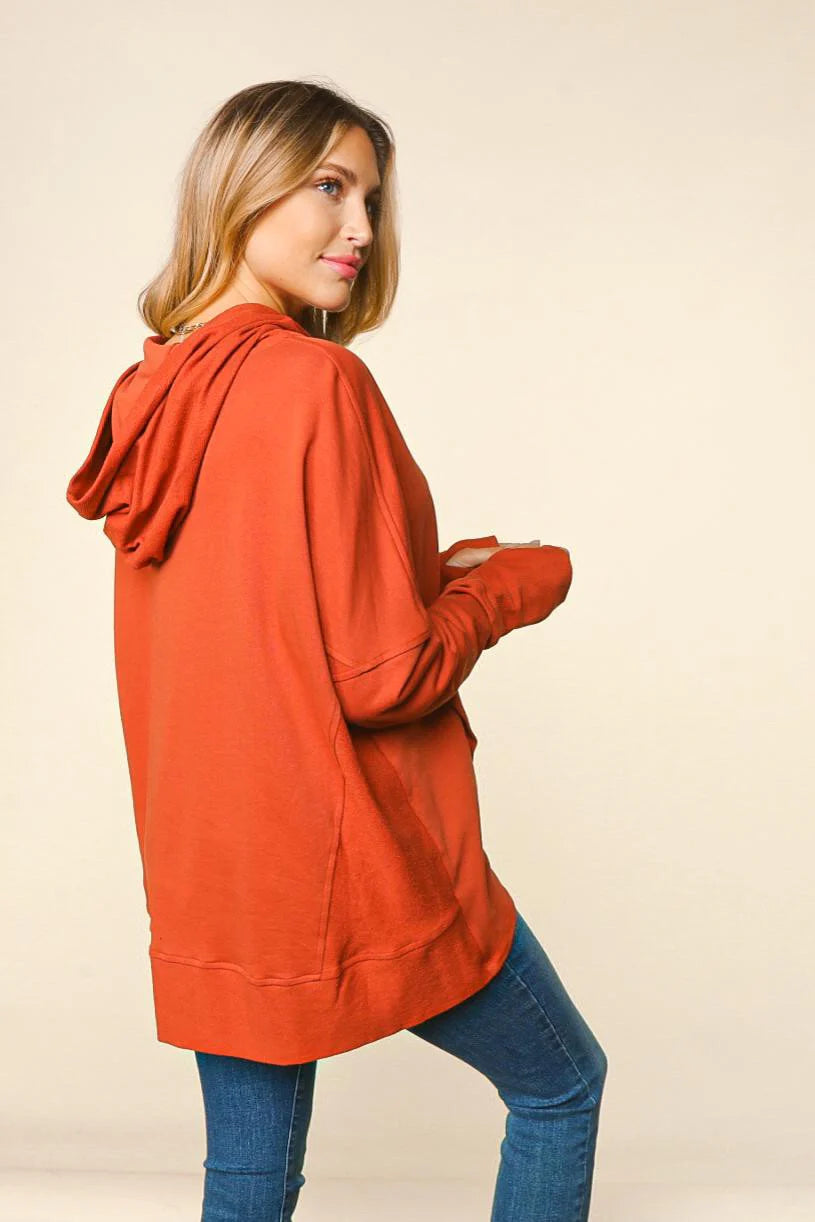 Woman wearing an orange hoodie and blue jeans on a beige background