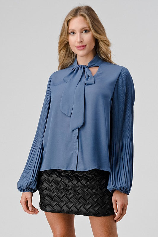 Woman wearing a blue blouse with a tie detail and black skirt on a gray background