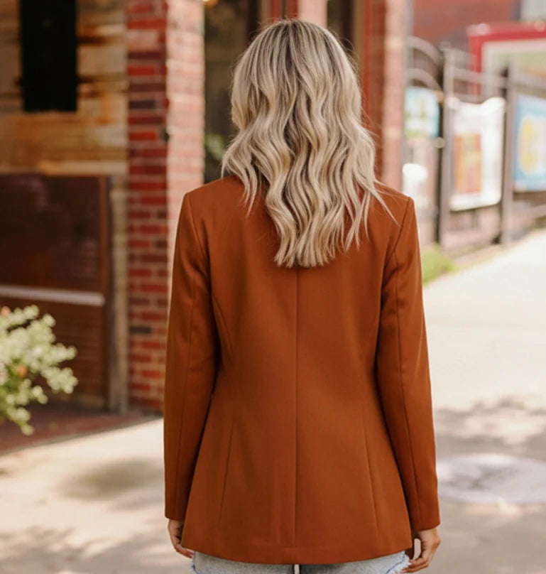 Person wearing a brown blazer and denim shorts on a sidewalk.