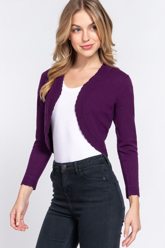 Woman wearing a purple cardigan over a white top and dark jeans on a light gray background