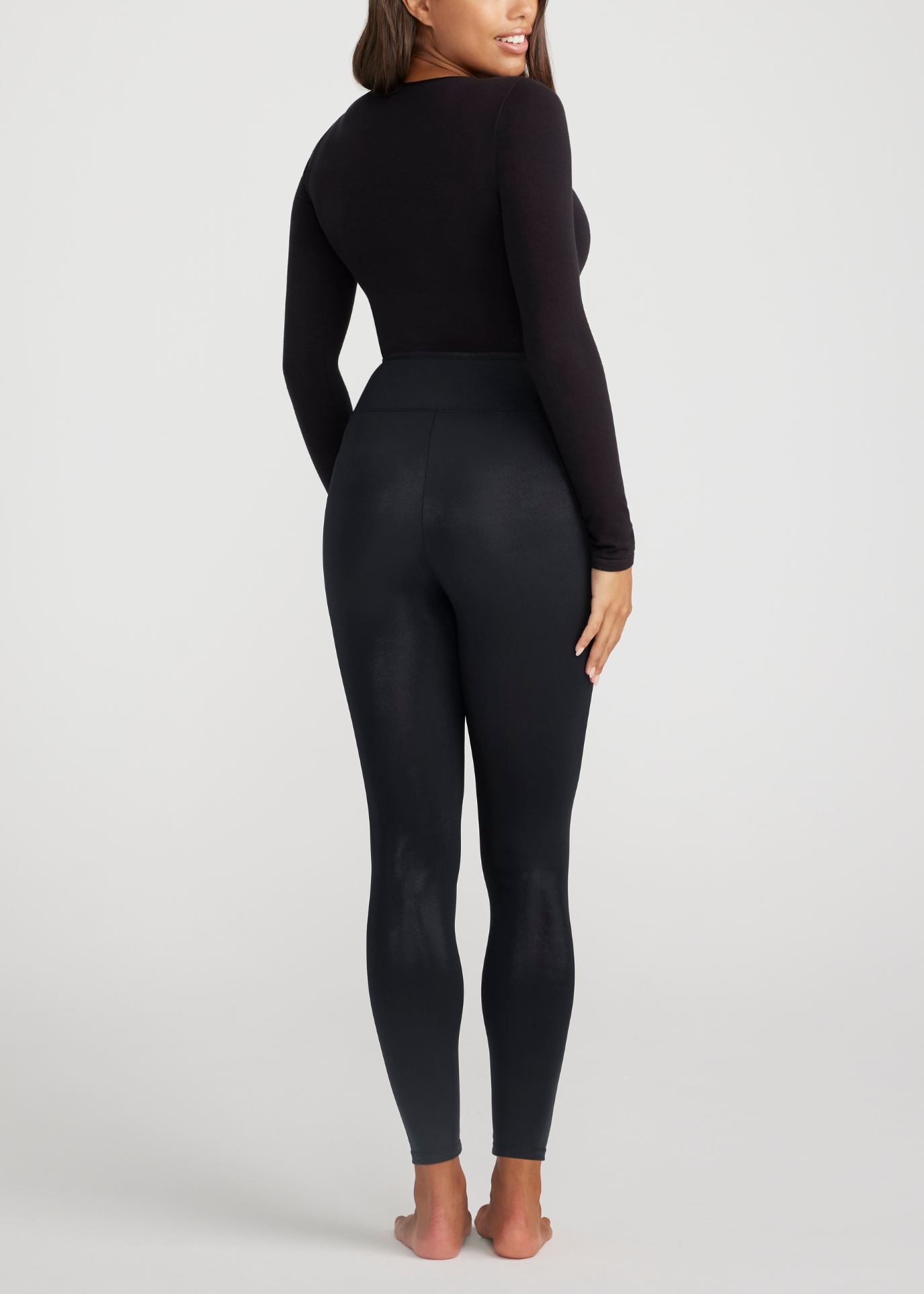 Person wearing a black long-sleeve top and leggings on a light gray background