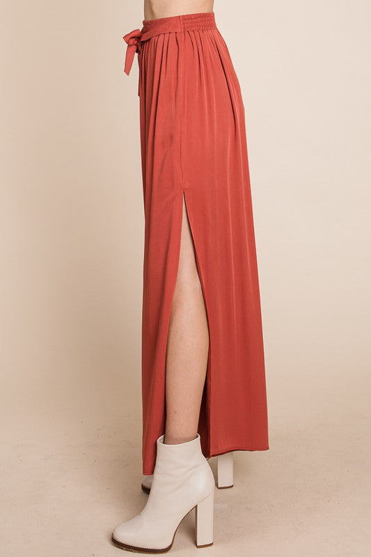 Rust pant with a high slit worn by a person, paired with white boots on a beige background