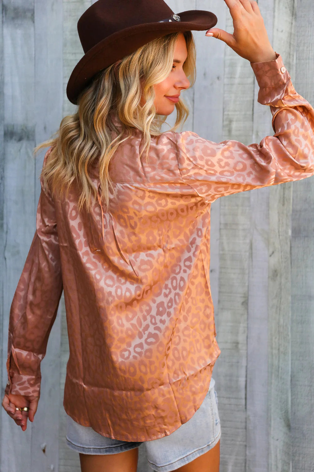 Woman wearing a brown patterned blouse and hat against a wooden background