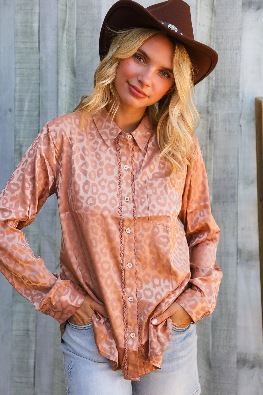 Woman wearing a patterned shirt and brown hat against a wooden background