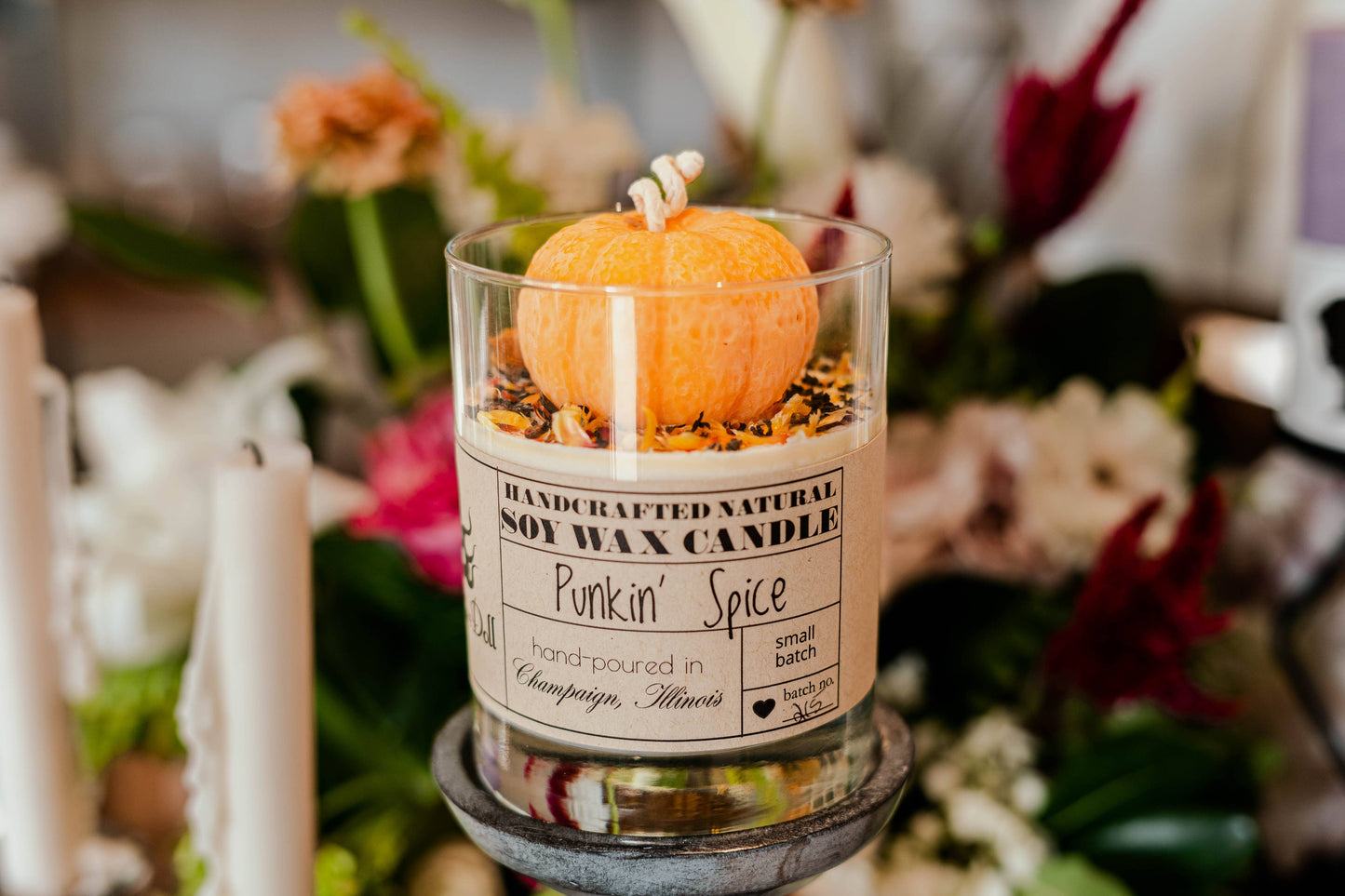 Pumpkin spice candle in a glass jar with decorative elements on a blurred floral background