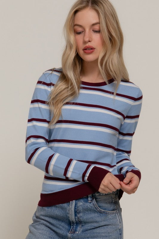Woman wearing a blue and burgundy striped sweater with jeans against a plain background