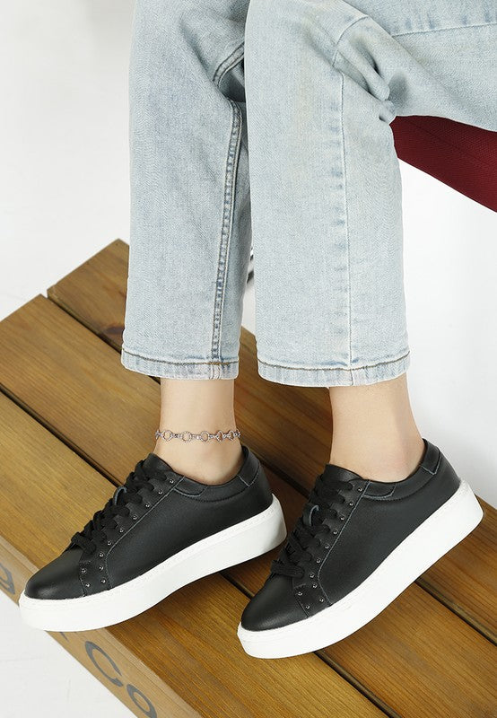 Person wearing black sneakers with white soles on a wooden floor.