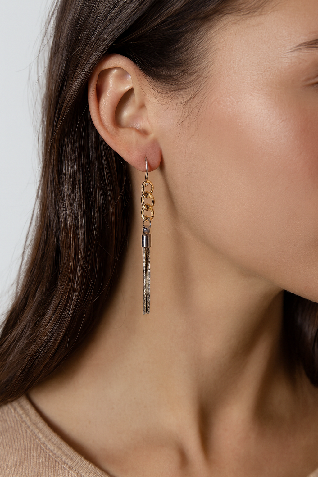 Close-up of a woman wearing gold tassel earrings with a neutral background