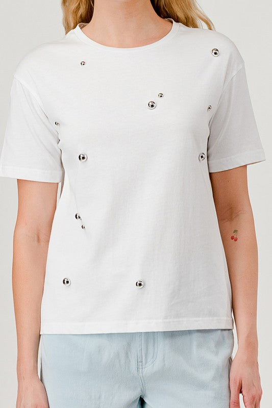 White t-shirt with decorative buttons worn by a person on a plain background