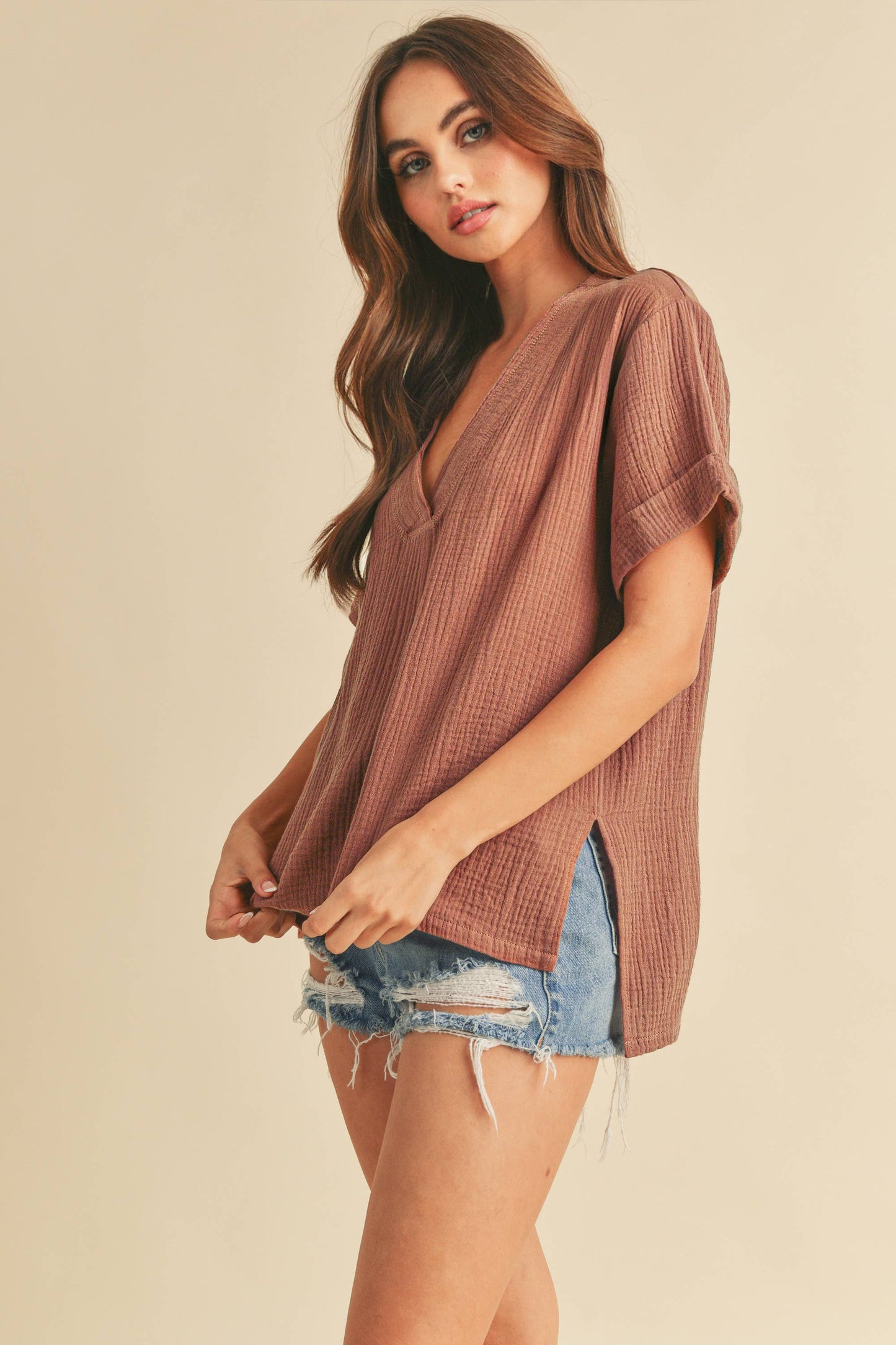 Woman wearing a brown ribbed top and denim shorts on a beige background