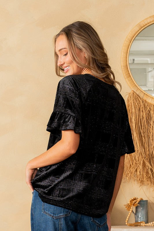 Woman wearing a black textured top and blue jeans in a room with a mirror and decorative items.