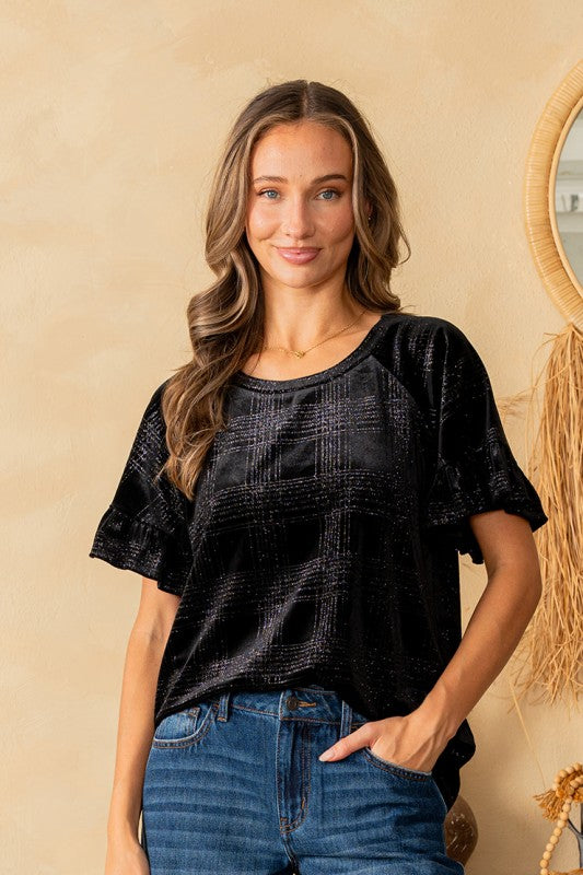 Woman wearing a black top and blue jeans against a beige wall.