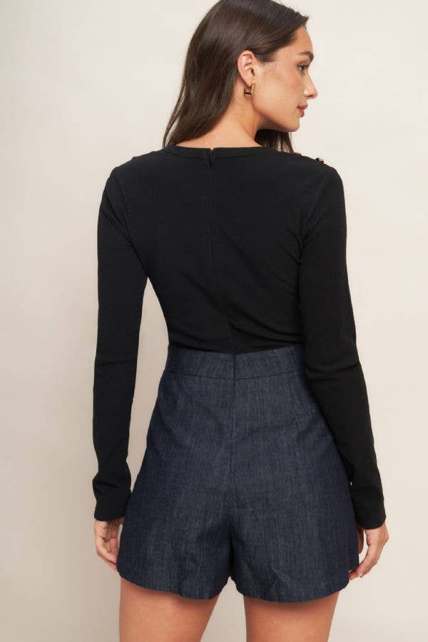 Woman wearing a black long-sleeve and dark denim shorts romper against a plain background