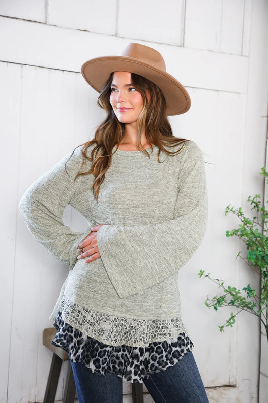 Woman wearing a long, light gray sweater with a leopard print hem, standing against a white brick wall.