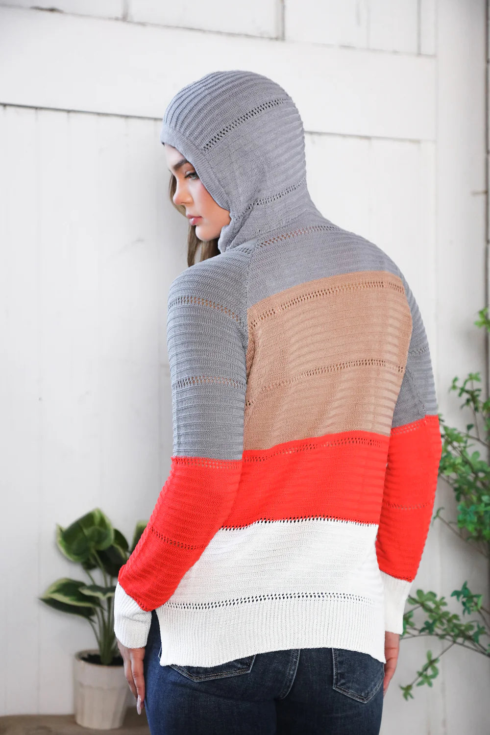 Person wearing a gray, brown, and red hooded sweater against a white wall.