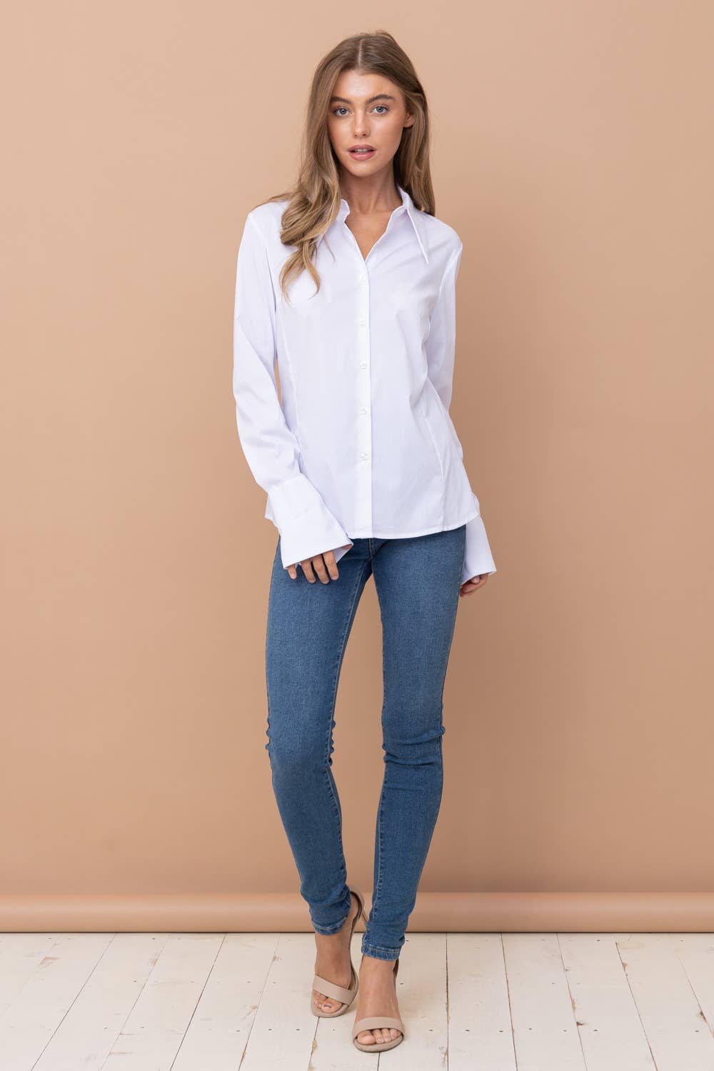 Woman wearing a white shirt and blue jeans against a beige wall.