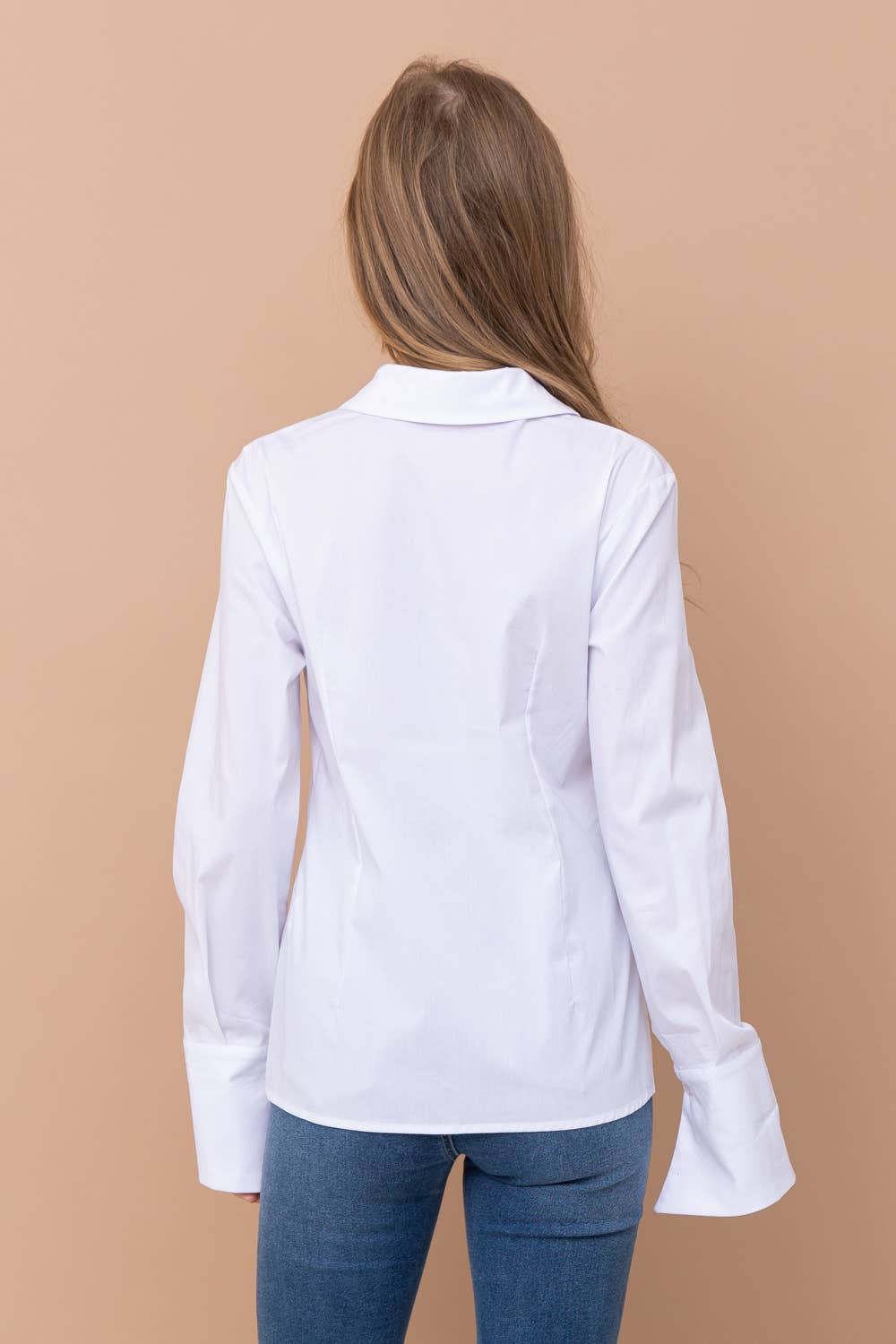 Person wearing a white blouse with long sleeves on a beige background