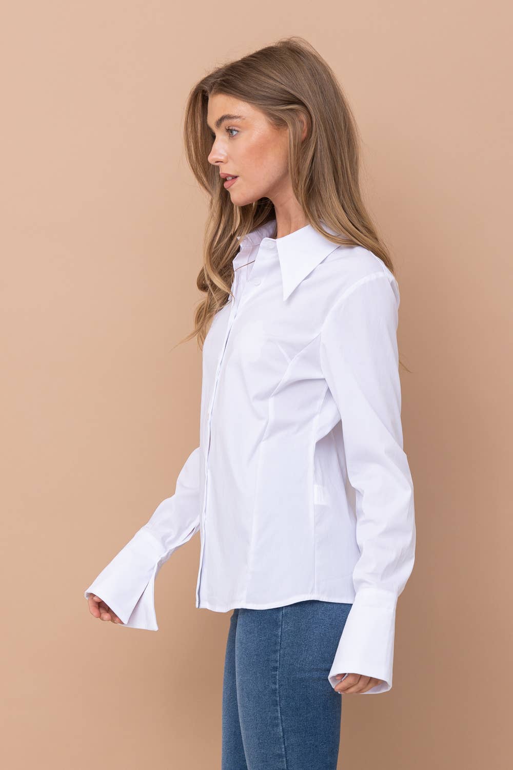 Woman wearing a white shirt and blue jeans against a beige background