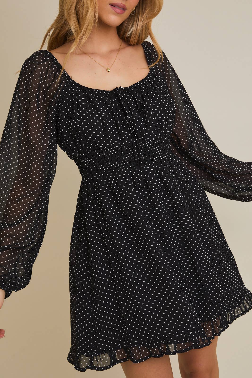 Black polka dot dress with sheer long sleeves on a neutral background