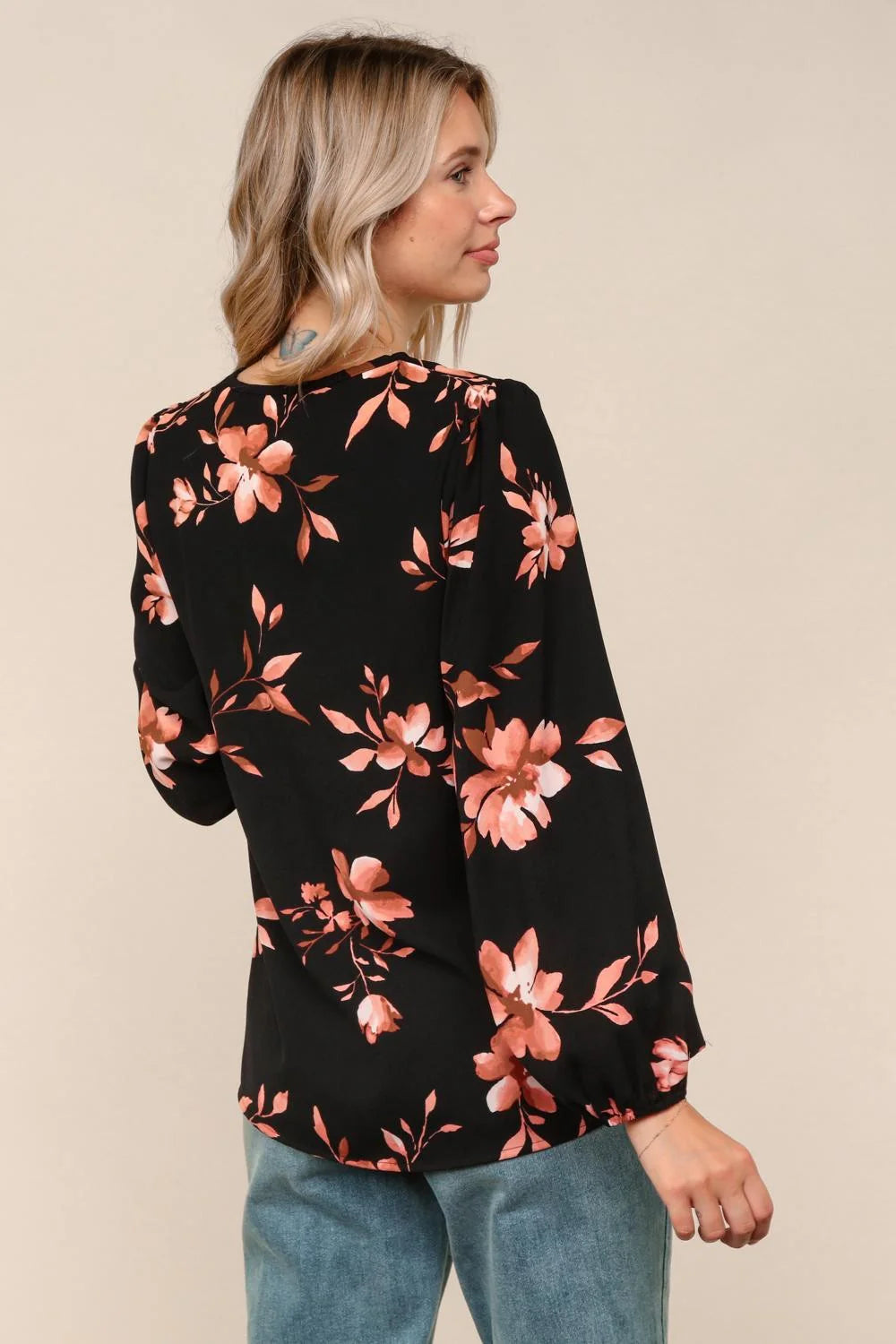 Woman wearing a black floral blouse with pink flowers on a beige background