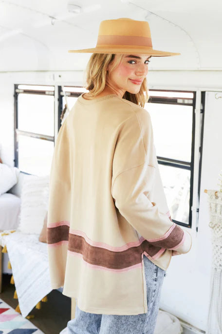 Woman wearing a beige cardigan with brown accents and a hat, standing in a bright room.