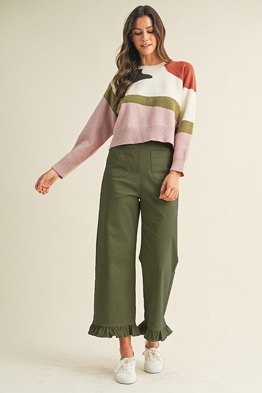 Woman wearing a colorful sweater and green pants on a beige background