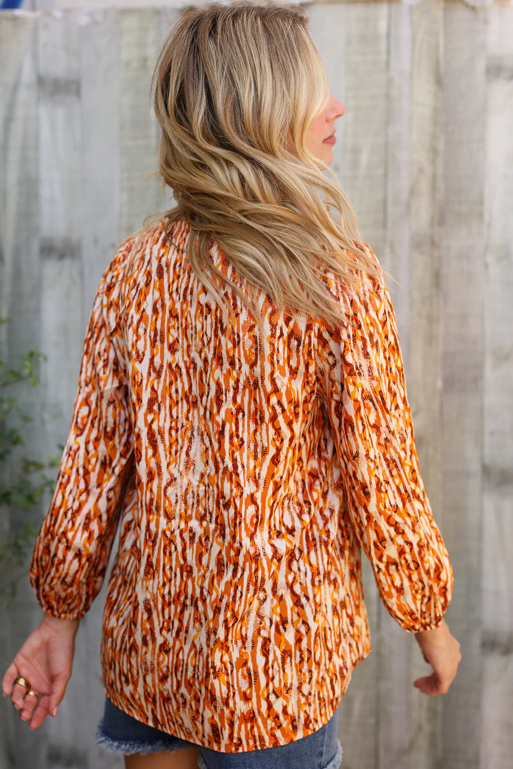 Person wearing an orange and white patterned blouse against a wooden fence background